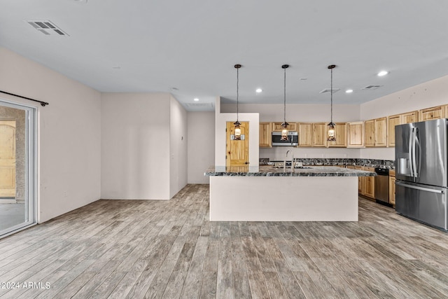 kitchen with decorative light fixtures, light brown cabinetry, an island with sink, appliances with stainless steel finishes, and light hardwood / wood-style flooring