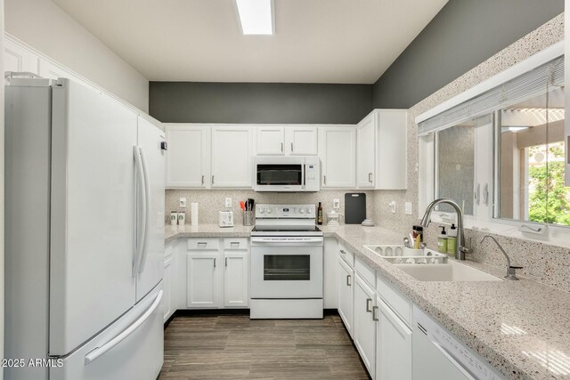 kitchen featuring backsplash, white appliances, white cabinetry, and a sink