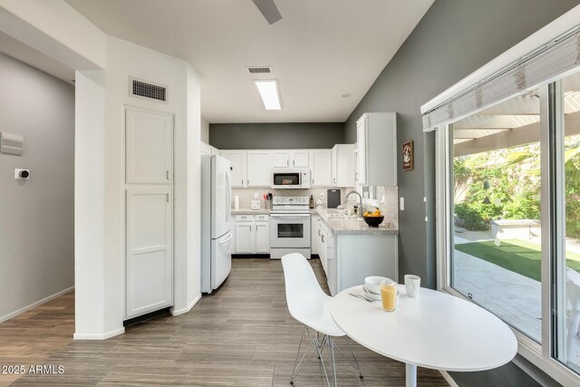 kitchen with white appliances, visible vents, a sink, decorative backsplash, and white cabinets