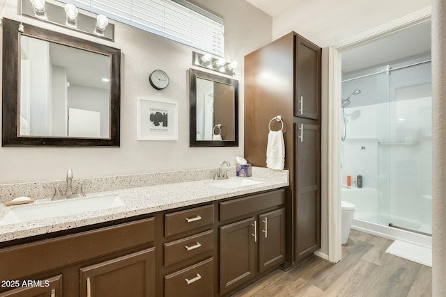 bathroom with toilet, wood finished floors, a stall shower, and a sink