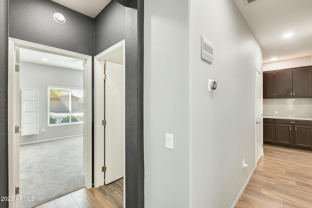 corridor featuring visible vents, baseboards, light wood-style floors, and light carpet