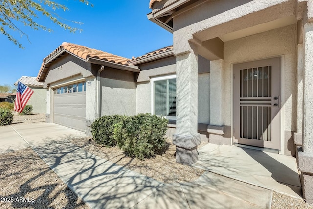 view of exterior entry featuring a tiled roof, a garage, driveway, and stucco siding