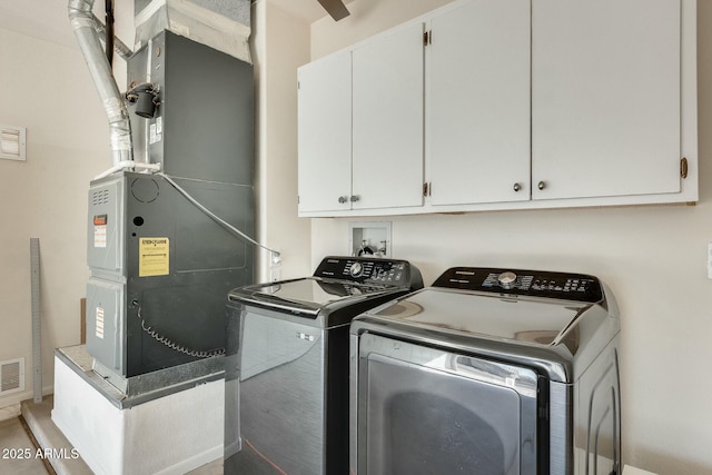 washroom with washing machine and clothes dryer, heating unit, cabinet space, and visible vents