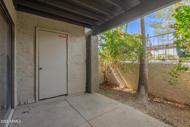 view of exterior entry with a patio area, fence, and stucco siding