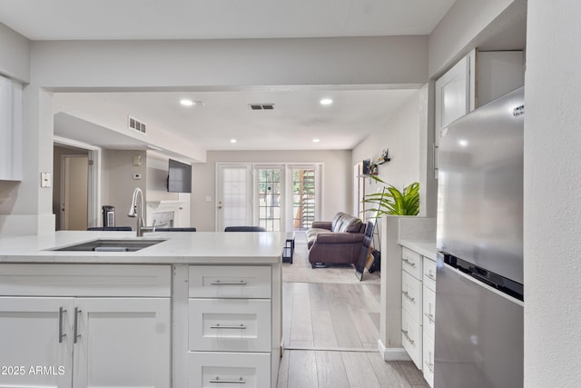 kitchen with freestanding refrigerator, white cabinetry, open floor plan, and a sink