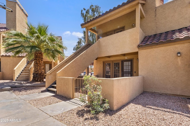 exterior space featuring fence, a tile roof, stucco siding, stairway, and a gate