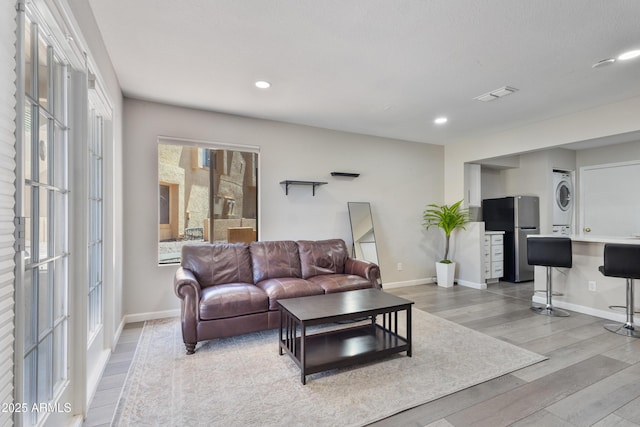 living room with recessed lighting, baseboards, light wood finished floors, and stacked washer / dryer