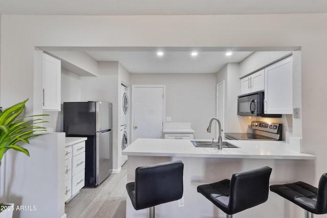 kitchen featuring a sink, stainless steel appliances, white cabinetry, a peninsula, and stacked washer / dryer