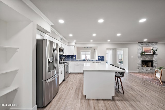 kitchen featuring a breakfast bar, a center island, white cabinets, a stone fireplace, and stainless steel appliances