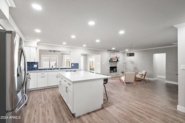 kitchen with a kitchen island, stainless steel refrigerator with ice dispenser, decorative backsplash, a fireplace, and white cabinets