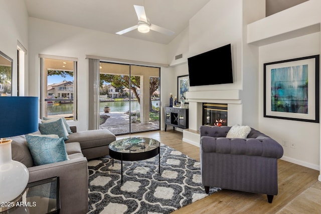 living room with a glass covered fireplace, high vaulted ceiling, baseboards, and wood finished floors