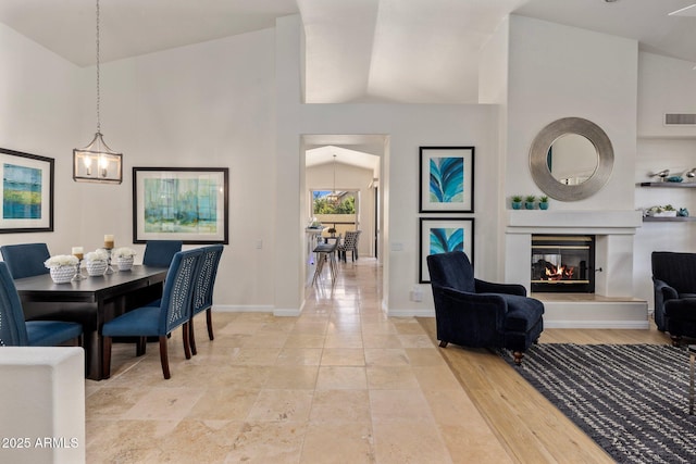 dining area featuring visible vents, light wood-type flooring, a glass covered fireplace, baseboards, and a towering ceiling