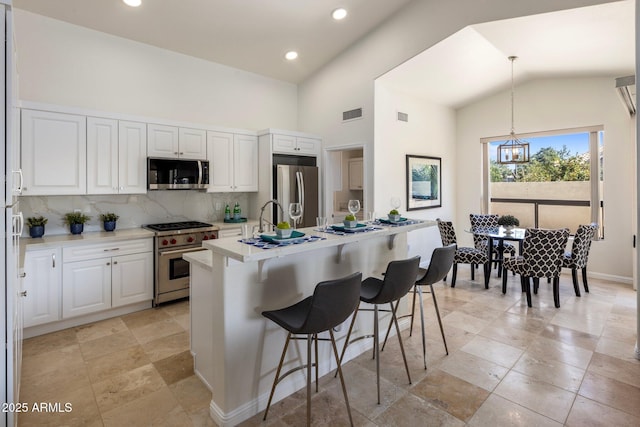 kitchen with a kitchen island with sink, appliances with stainless steel finishes, white cabinets, light countertops, and decorative backsplash