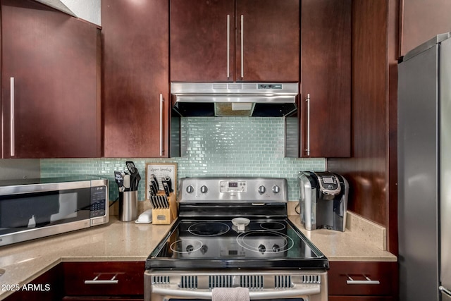 kitchen with under cabinet range hood, stainless steel appliances, backsplash, and light stone countertops