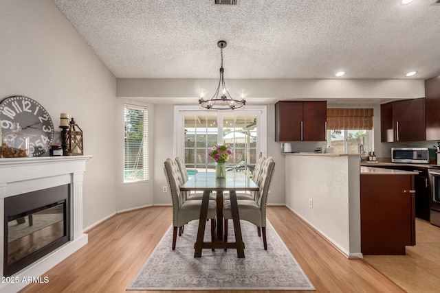 dining space featuring a textured ceiling, a chandelier, light wood finished floors, a glass covered fireplace, and baseboards