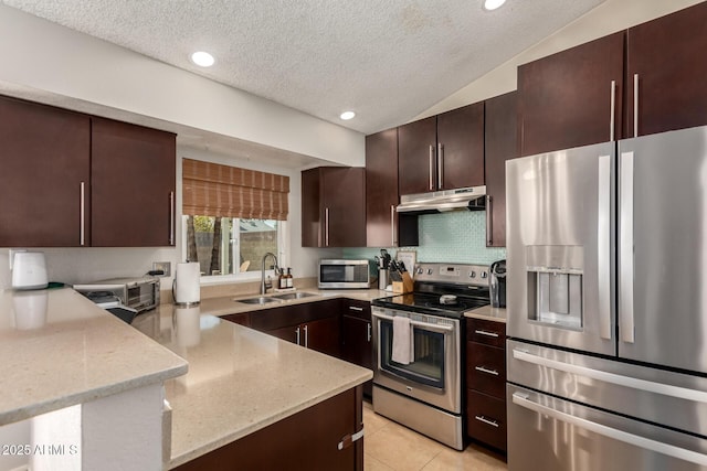 kitchen with appliances with stainless steel finishes, a sink, under cabinet range hood, a textured ceiling, and a peninsula