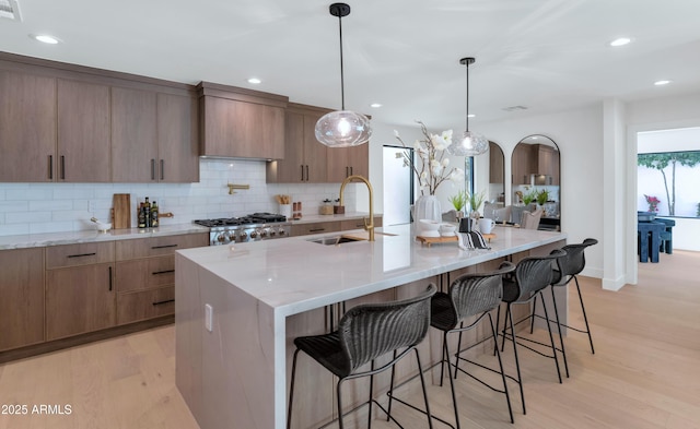 kitchen featuring light wood-style flooring, light stone counters, a sink, a kitchen bar, and backsplash