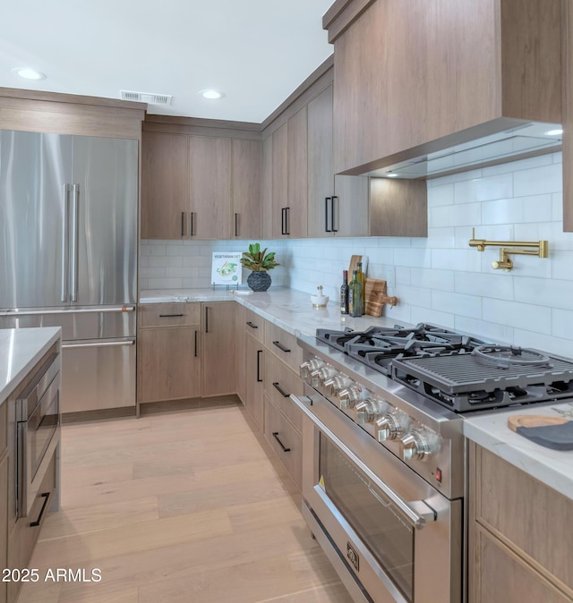 kitchen featuring light stone counters, high end appliances, visible vents, light brown cabinets, and premium range hood