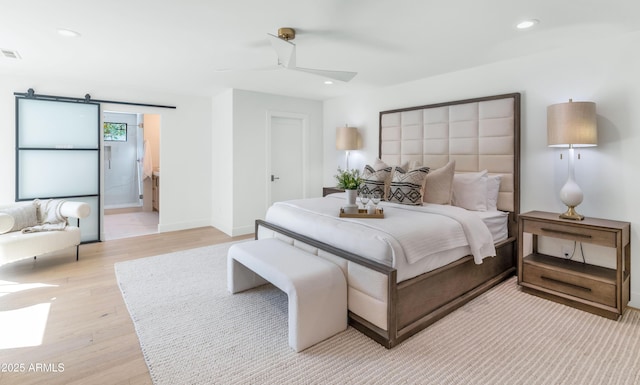 bedroom with recessed lighting, visible vents, a barn door, light wood-type flooring, and baseboards