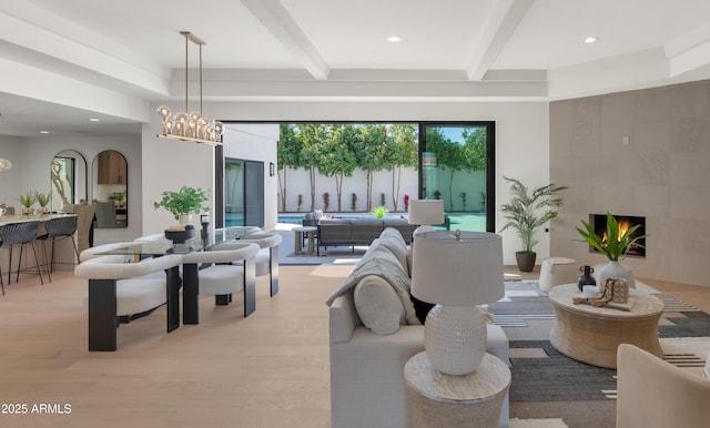 living area with a chandelier, beamed ceiling, a tile fireplace, and light wood-style flooring