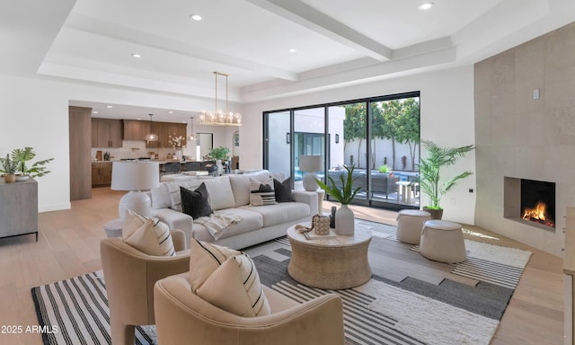 living room featuring light wood-type flooring, beam ceiling, a notable chandelier, and a premium fireplace