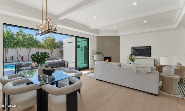 dining area featuring a wealth of natural light, a premium fireplace, beamed ceiling, light wood-style floors, and a notable chandelier