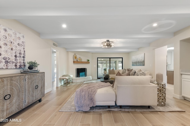 living area with wood tiled floor, visible vents, a fireplace with raised hearth, and beam ceiling