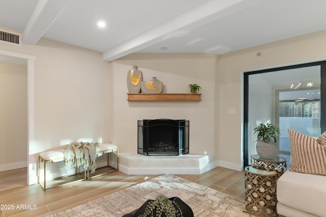 living room featuring a fireplace with raised hearth, visible vents, wood tiled floor, beamed ceiling, and baseboards