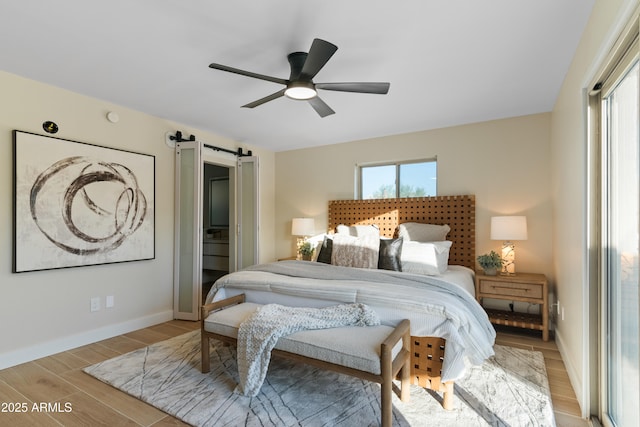 bedroom with a barn door, baseboards, ceiling fan, and wood finished floors