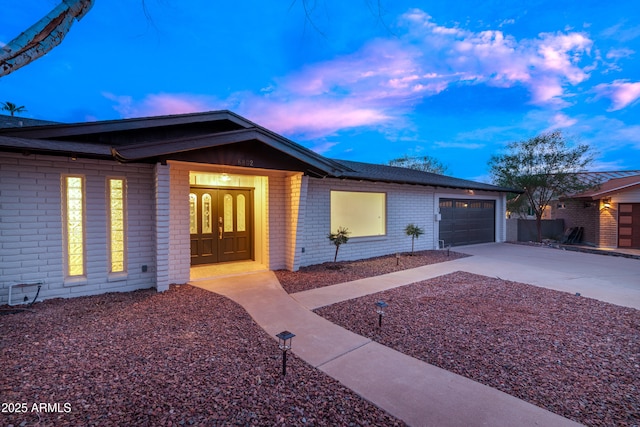 ranch-style home with an attached garage, concrete driveway, french doors, and brick siding