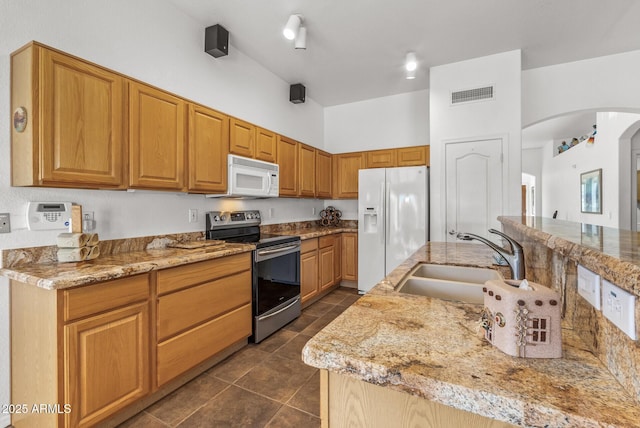 kitchen featuring sink, light stone counters, white appliances, and a towering ceiling