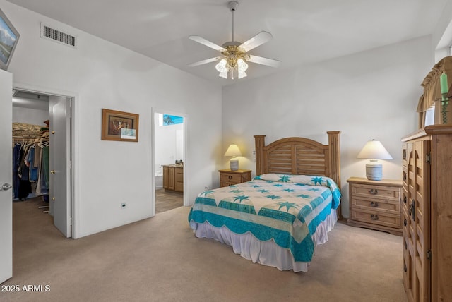 bedroom with a spacious closet, light colored carpet, ensuite bath, and a closet