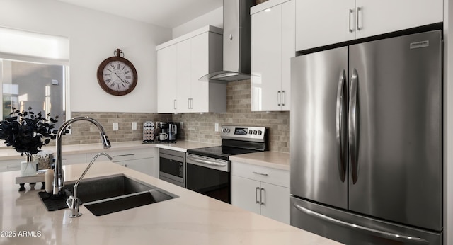 kitchen with wall chimney exhaust hood, tasteful backsplash, white cabinetry, appliances with stainless steel finishes, and sink