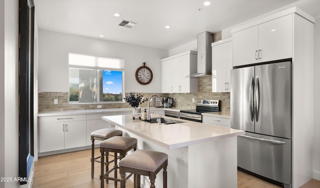 kitchen featuring a center island with sink, appliances with stainless steel finishes, wall chimney range hood, and a breakfast bar area