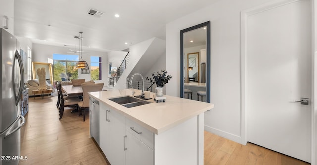 kitchen featuring a center island with sink, appliances with stainless steel finishes, white cabinets, decorative light fixtures, and sink