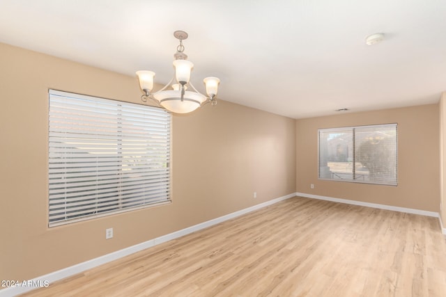 unfurnished room featuring a notable chandelier and light hardwood / wood-style flooring