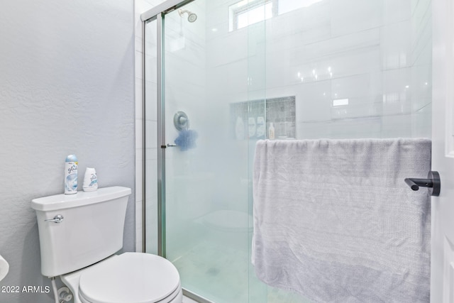 bathroom featuring toilet and a shower with shower door