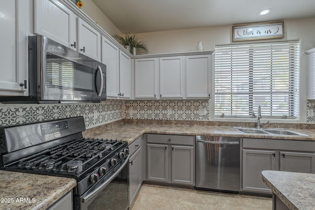 kitchen featuring light tile patterned floors, stainless steel appliances, a sink, gray cabinets, and backsplash