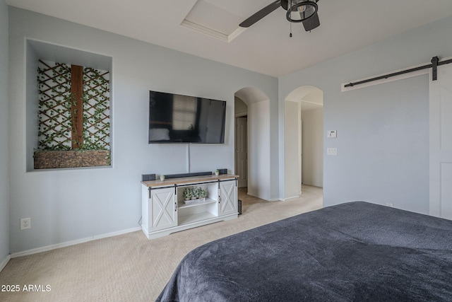 unfurnished bedroom featuring light carpet, a barn door, baseboards, arched walkways, and a ceiling fan