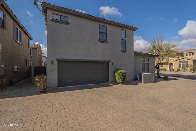 mediterranean / spanish house featuring a garage, a residential view, a tiled roof, decorative driveway, and stucco siding