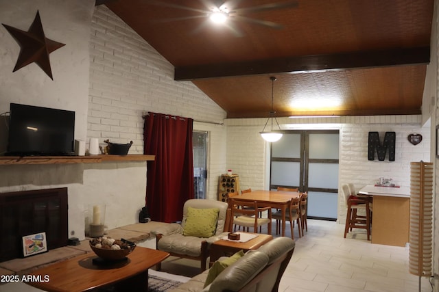 living room with brick wall, vaulted ceiling with beams, a glass covered fireplace, and ceiling fan