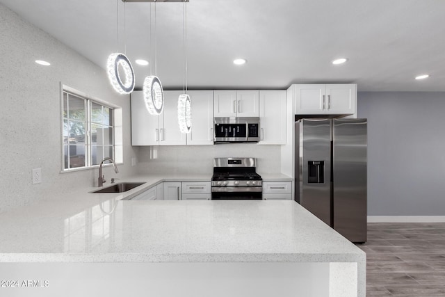 kitchen with pendant lighting, white cabinets, sink, appliances with stainless steel finishes, and light hardwood / wood-style floors