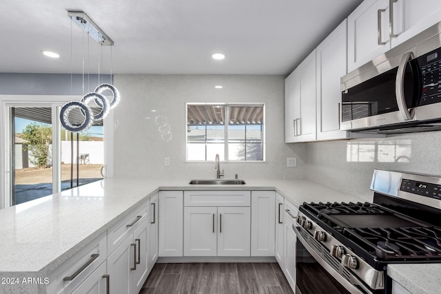 kitchen with sink, appliances with stainless steel finishes, decorative light fixtures, white cabinetry, and wood-type flooring