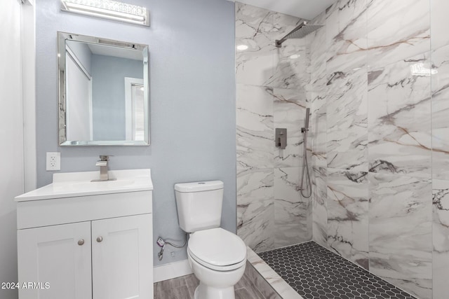 bathroom with vanity, toilet, a tile shower, and wood-type flooring