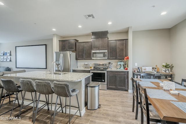 kitchen featuring a kitchen bar, appliances with stainless steel finishes, sink, dark brown cabinets, and a center island with sink