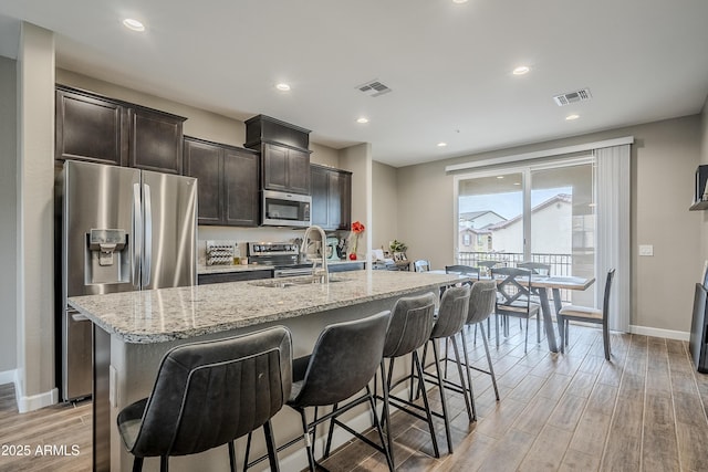 kitchen featuring light stone countertops, dark brown cabinetry, appliances with stainless steel finishes, an island with sink, and sink