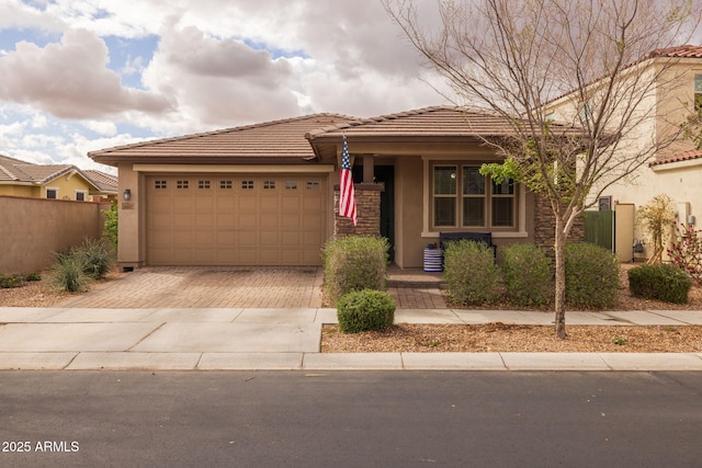 view of front facade featuring fence, a tile roof, stucco siding, decorative driveway, and an attached garage