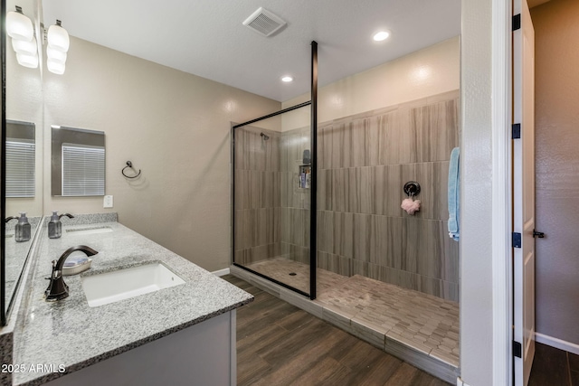 full bath with visible vents, a sink, wood finished floors, a tile shower, and double vanity