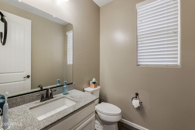 half bathroom featuring baseboards, toilet, vanity, and a textured wall