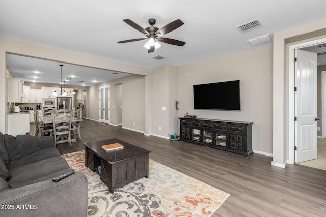 living room featuring visible vents, baseboards, wood finished floors, and ceiling fan with notable chandelier